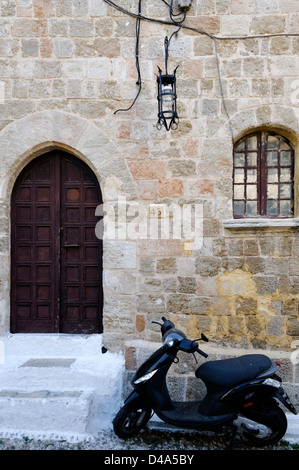 Rodas. Grecia. Moto o scooter en frente de un antiguo edificio de piedra con un umbral arqueado y windows.