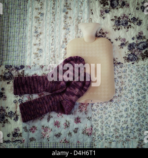Botella de agua caliente con calcetines tejidos a mano en una cama vintage