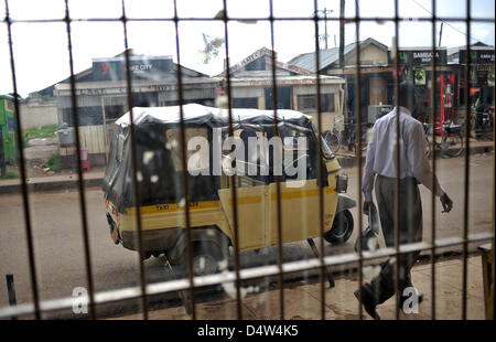 Un peatón camina pasado un tuk tuk en Kisumu, Kenya, 29 de octubre de 2009. Dos a tres pasajeros encajan en los vehículos de tres ruedas, que se utilizan a menudo como taxis y generalmente son el medio más económico de transporte en la ciudad. Foto: Andreas Gebert Foto de stock