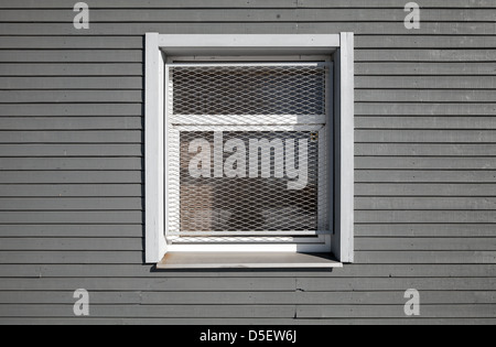 La textura de una ventana está bloqueada con rejilla de metal en la pared de madera gris Foto de stock