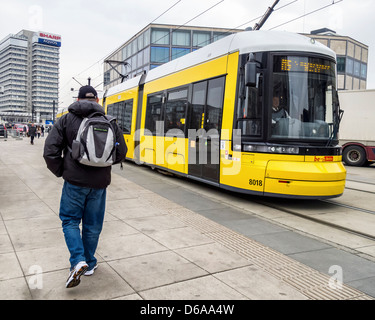 Altos hombre vestido con pantalones vaqueros caminando hacia un tranvía amarillo en Alexanderplatz, Mitte, Berlin Foto de stock