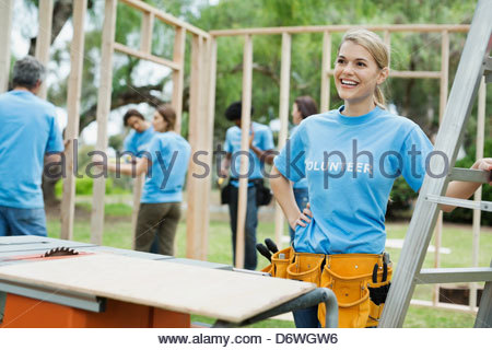 Feliz joven por voluntarios de la escalera con marco de madera en el fondo de construcción