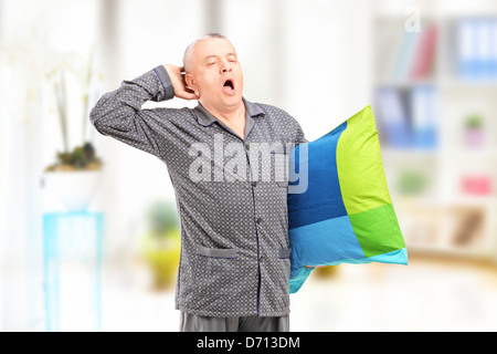 Un soñoliento hombre maduro en pijama sosteniendo una almohada y bostezos en casa