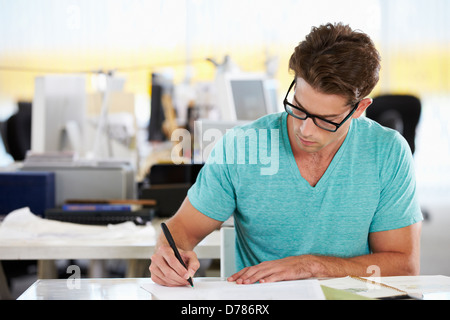 Hombre escrito en un escritorio en la ajetreada oficina creativa Foto de stock