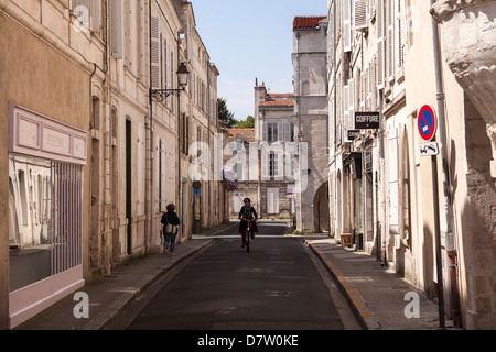 Los ciclos de una mujer en una calle lateral en la ciudad vieja de La Rochelle, Francia Foto de stock