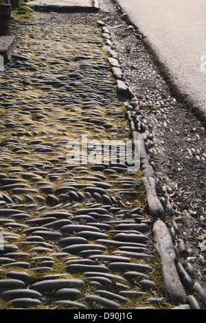 Piedras colocadas en patrones lineales y espiguilla para formar el pavimento y canalones fuera de una terraza de casas, Llanrhystud, Gales, Reino Unido.