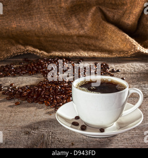 Café y fondo rústico - café taza y plato lleno de espresso, con granos de café y saco de henequen detrás, Foto de stock