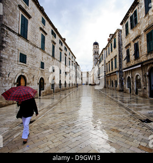 Señora camina a través de las calles húmedas brillante al amanecer en Dubrovnik Foto de stock