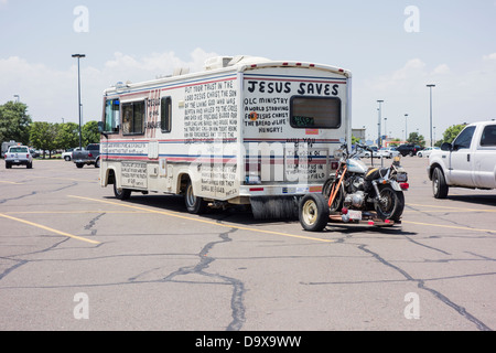 Un viejo vehículo recreativo remolcando una moto y pintado a mano con las escrituras bíblicas se asienta en un parking. Foto de stock