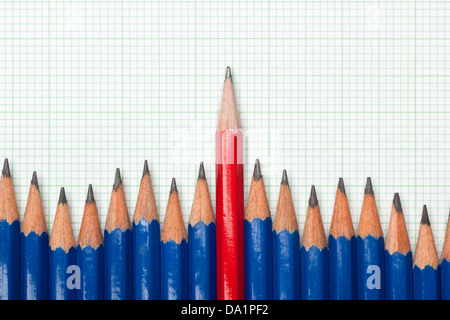 Lápiz rojo que sobresalían desde una fila de lápices de color azul sobre un trozo de papel milimetrado Foto de stock
