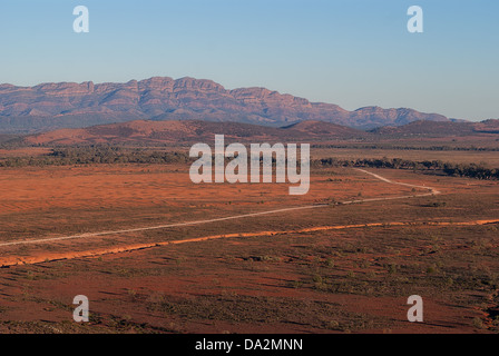 Un polvoriento camino serpentea outback bushland hacia gamas distantes ajuste iluminado por el sol. Foto de stock