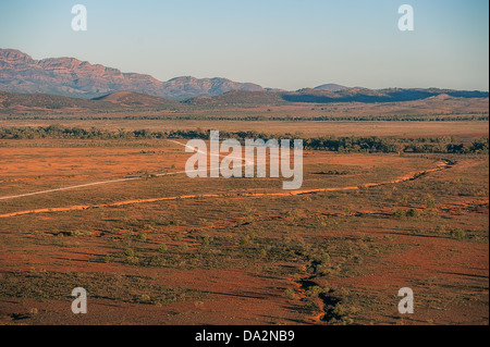 Un polvoriento camino serpentea outback bushland hacia gamas distantes ajuste iluminado por el sol. Foto de stock