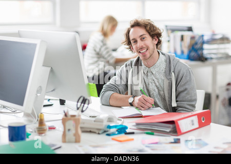 Hombre joven sentado en la mesa y sonriendo en la oficina creativa, Retrato