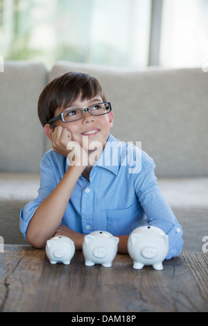 Muchacho sentado con hucha en mesa de café Foto de stock