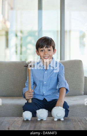 Niño sosteniendo un martillo para aplastar hucha Foto de stock