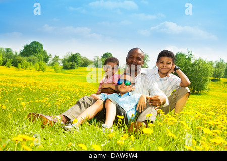 Feliz padre con sus hijos sentados en el césped en el parque el día soleado