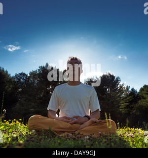 Hombre chino meditar al aire libre durante el amanecer en la naturaleza, sentarse con las piernas cruzadas sobre el césped bajo un cielo azul