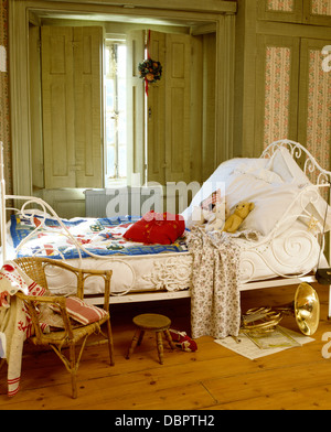 Almohadas y edredón blanco azul en la Antigua cama de hierro forjado en frente de la ventana con persianas pintadas en dormitorio infantil Foto de stock