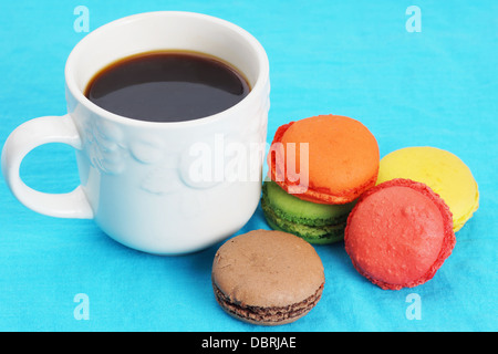 Taza de café negro y coloridos macarons sobre azul Foto de stock