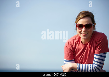 Retrato de mujer joven llevaba gafas de sol con forma de corazón en la costa Foto de stock