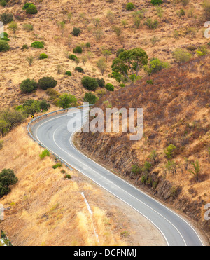 Serpenteante carretera asfaltada en el campo, serpenteando a través de terreno montañoso seco visto desde arriba Foto de stock