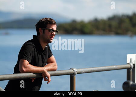 Un hombre joven con gafas de sol miradas sobre el agua desde el embarcadero Luss Loch Lomond, Escocia, Reino Unido Foto de stock