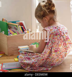 Niña sentada en el piso leyendo libros Foto de stock
