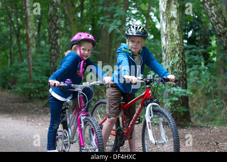 Dos niños, niño y niña, con edades comprendidas entre 6 y 8 en sus motos / bicicletas en un bosque / madera / Rastro / estacionamiento Foto de stock