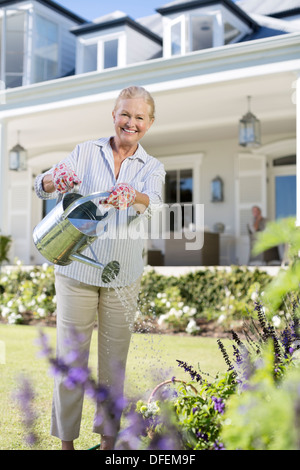 Retrato de mujer senior sonriente regar las flores en el jardín Foto de stock