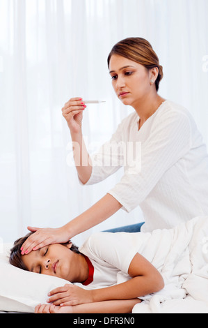 Mujer controlar la fiebre de su hijo con un termómetro Foto de stock