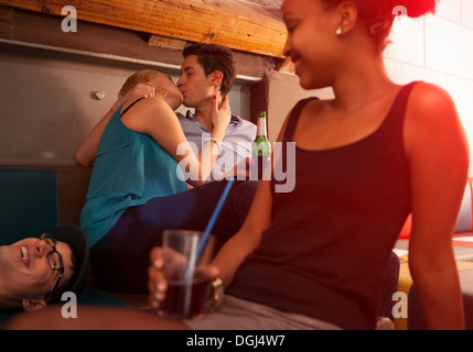 Joven pareja besándose, amigos sentado cerca Foto de stock