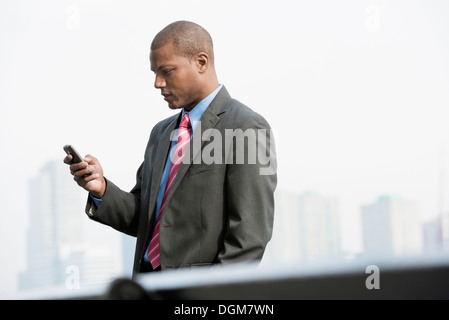 Un hombre joven en un traje de negocios con una camisa azul y corbata roja. En una calle de la ciudad de Nueva York. Utilizando un teléfono inteligente.