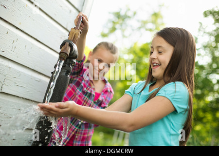 Granja orgánica. Dos niñas lavando sus manos bajo el flujo de agua de una bomba en el patio. Foto de stock