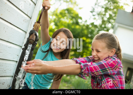 Granja orgánica. Dos niñas lavando sus manos bajo el flujo de agua de una bomba en el patio. Foto de stock