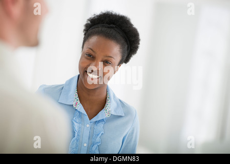 Oficina interior. Una mujer sonriendo y hablando con un hombre. Foto de stock
