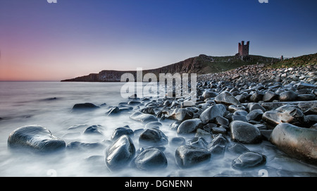 Playa de guijarros con ruinas de castillos en el fondo Foto de stock