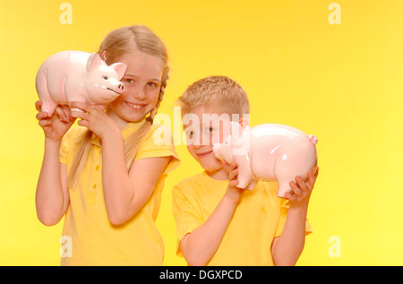 Chico y chica, hermano y hermana, sonriente, sosteniendo hucha Foto de stock