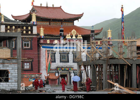 Los monjes tibetanos en hábitos rojos pararse y caminar bajo la lluvia a través de la obra de construcción al monasterio Lhagang Foto de stock