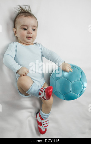 Un bebé bebé niño usando zapatos de fútbol junto a un balón de fútbol stock - Alamy