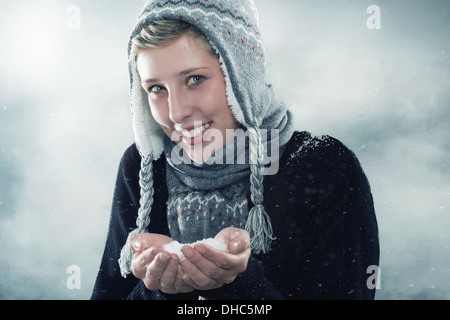 Feliz joven mujer vistiendo ropas invernales mostrando una mano llena de nieve