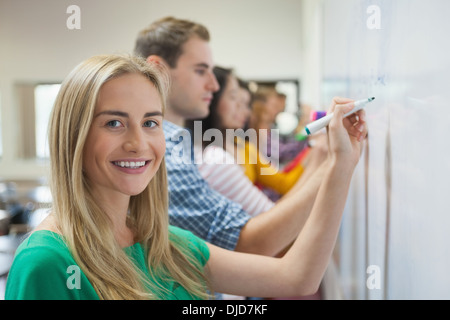 Los estudiantes escrito en la pizarra junto en la clase con una sonrisa en la cámara Foto de stock