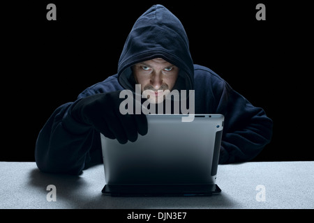 Un hombre encapuchado utilizando un equipo de tableta representa un cyber criminales. Foto de stock