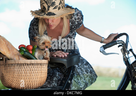 Mujer madura en bicicleta eléctrica con perro y hortalizas en la cesta