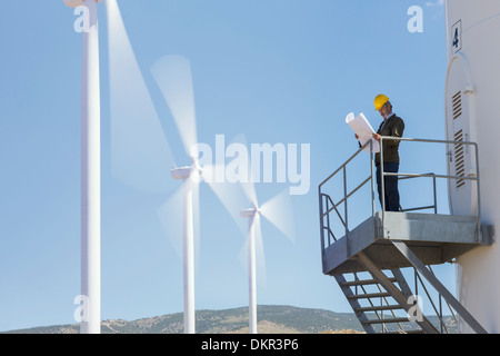 Empresario examinar blueprints por turbinas de viento en el paisaje rural Foto de stock