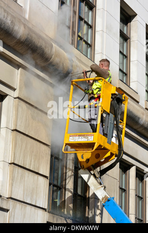Obrero en cherry picker grúa con chorro de agua a alta presión para limpiar la fachada de piedra del edificio de oficinas Foto de stock