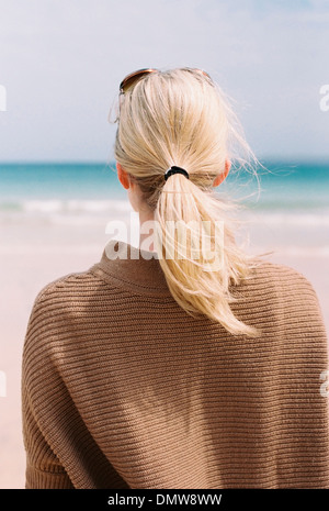 Una mujer de pelo rubio mirando al mar desde la orilla.