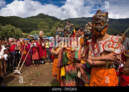 Bhután, Bumthang Thangbi Mani Lhakang Tsechu Festival, bailarines enmascarados en traje con monjes jugando mucho dungchen trompetas. Foto de stock