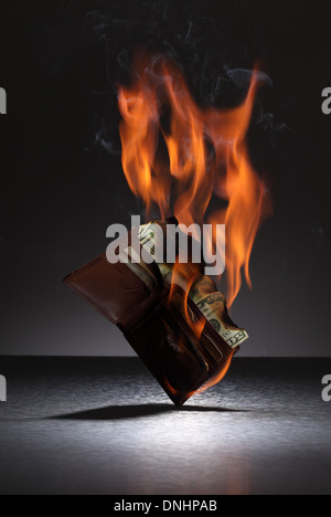 Una cartera de cuero marrón llena de tarjetas de crédito y dinero en fuego. Foto de stock