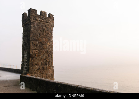 Castlated torre de piedra sobre un mar un muro en una mañana brumosa