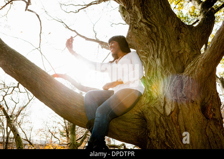 Mujer joven tomando autorretrato sentado en el árbol del parque
